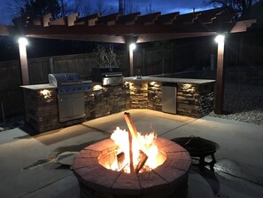 An outdoor kitchen with a stone fireplace, a grill, and a sink.