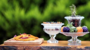 Una mesa de madera con diversos alimentos, incluyendo un tazón de fruta y un recipiente de vidrio con una planta.