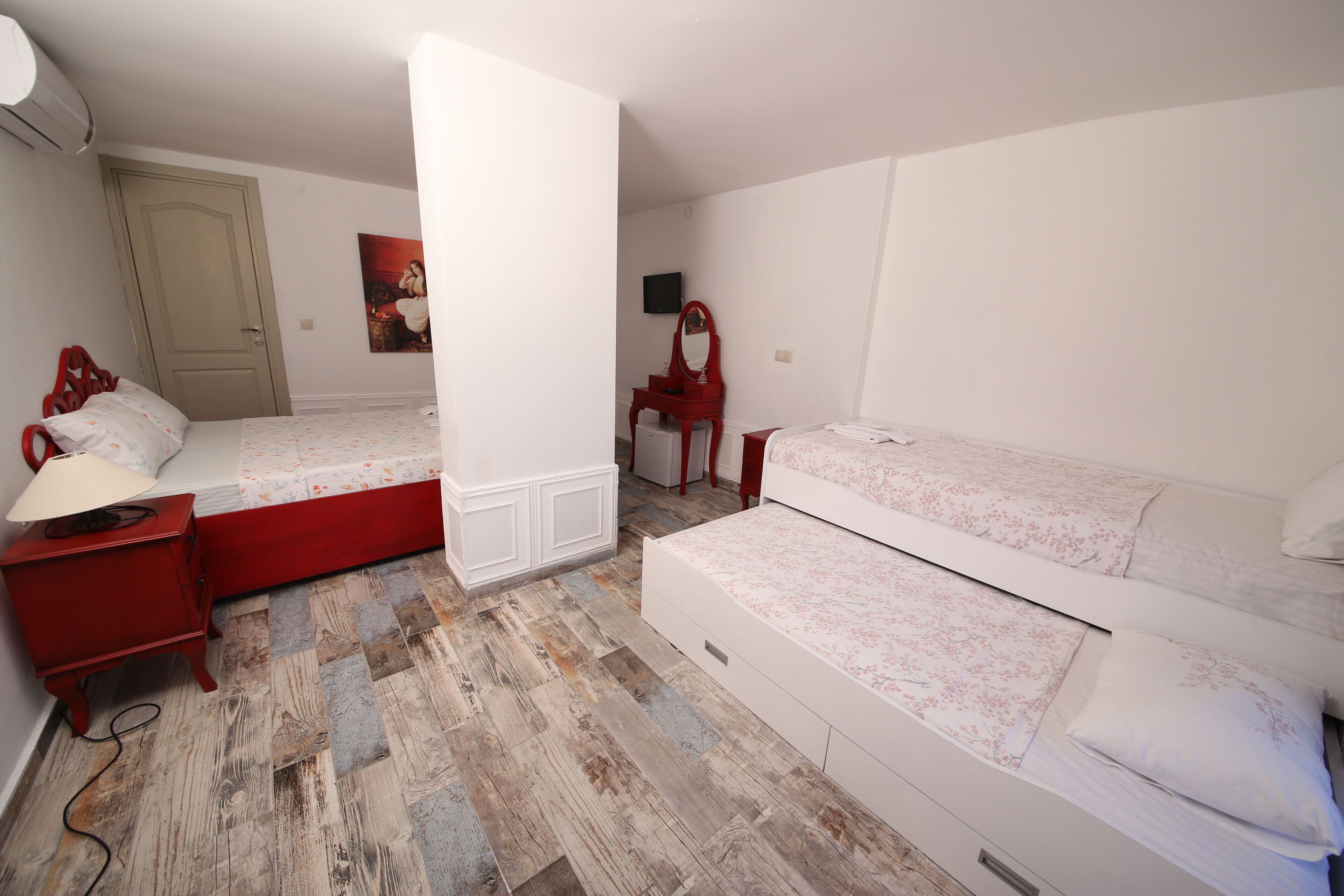 Une chambre avec deux lits, une commode rouge, un miroir et un tableau accroché au mur.