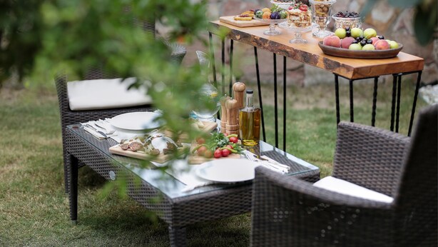 Mobiliario de comedor exterior con mesa y sillas de mimbre, y una variedad de comida y bebidas.