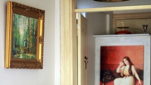 Una habitación con una mesa de madera que muestra botellas, un cuadro enmarco y una puerta que da a otra habitación con un cuadro rojo.