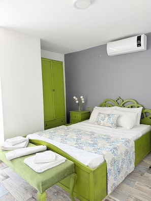 A bedroom with a green bed, white bedding, a green nightstand, a green wardrobe, and an air conditioning unit on the wall. - Cunda Morisi Otel (Ayvalik)