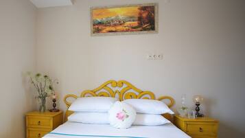 A bedroom with a bed, two nightstands, a vase with flowers, a painting on the wall, and a window.