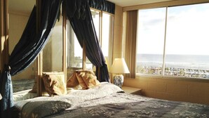 Una habitación de hotel con una cama grande, una mesita de noche, una lámpara y vistas a la playa y al océano.