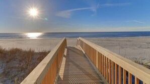 Eine Holzpromenade führt zu einem Strand mit blauem Himmel und Sonnenschein.