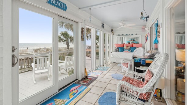 Ein raum im Strandstil mit Blick auf das Meer, ein weißes Rattangeflechtsofa und ein Essbereich mit Tisch und Stühlen.