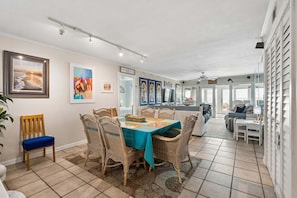 Un comedor con una mesa dispuesta para seis personas, rodeada de sillas de mimbre, un mantel azul y cuadros en las paredes.