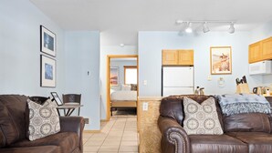 Ein modernes Wohnzimmer mit zwei braunen Ledersofas, einem Holztisch und einer Küchenzeile mit Holzschränken und einer Mikrowelle.