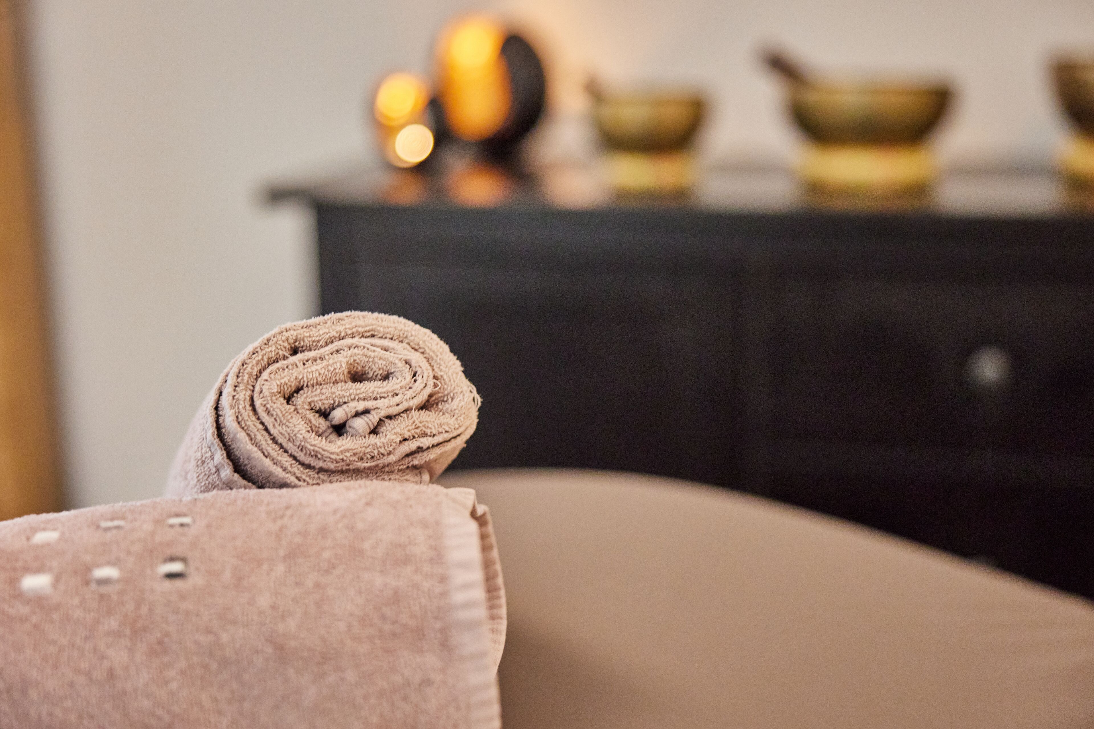 A rolled towel on a beige chair in a room with a dark-colored cabinet in the background.