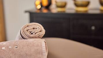 A rolled towel on a beige chair in a room with a dark-colored cabinet in the background.