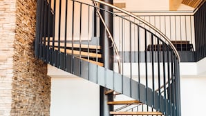 Una escalera de caracol con barandilla de metal negro, escalones de madera y una pared de ladrillo a un lado.