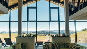 Amplia habitación con ventanas grandes que ofrecen vistas a un paisaje montañoso. Hay dos sofás de estampado verde y una pequeña mesa en el centro.
