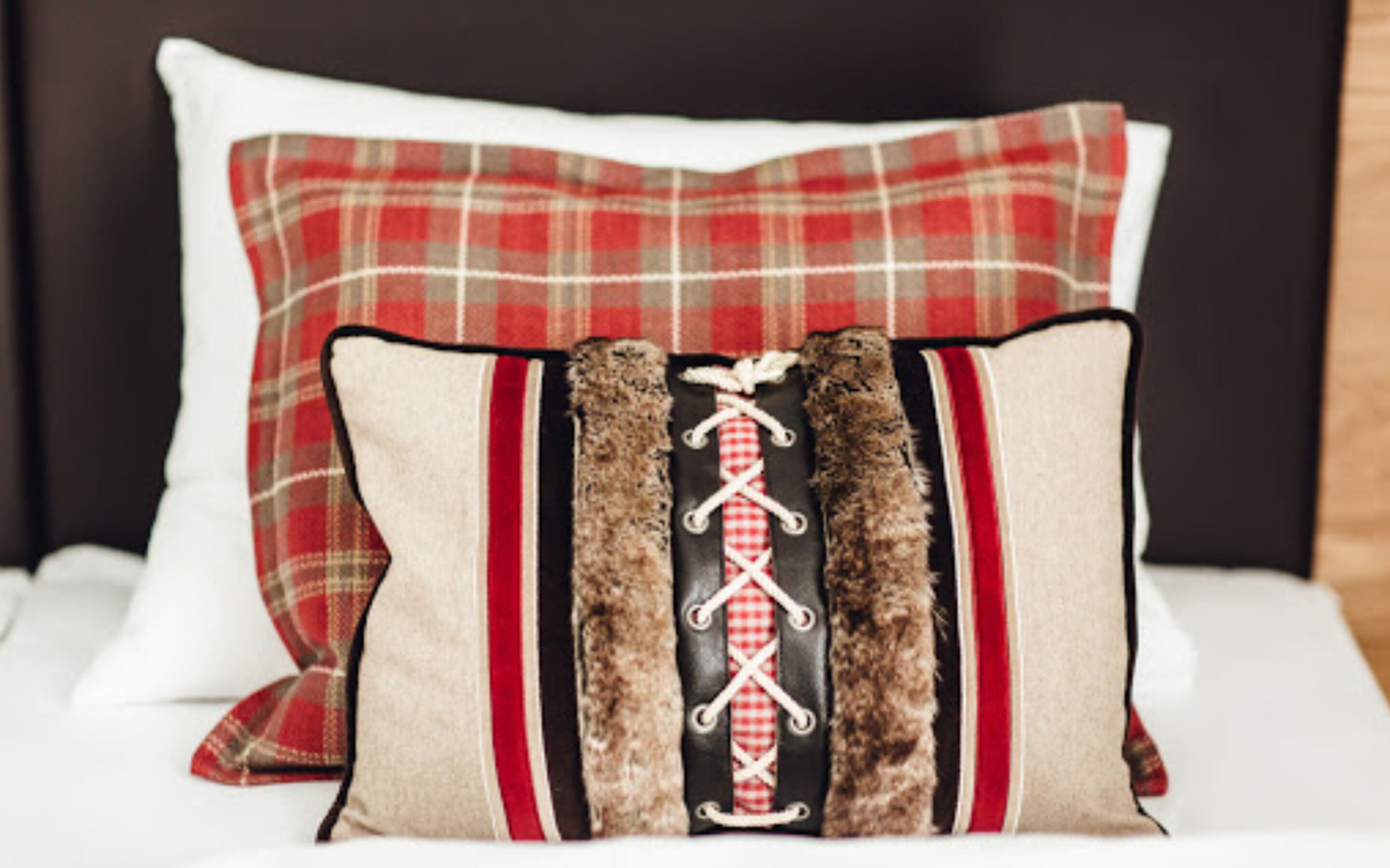 Una cama con dos almohadas, una con estampado escocés y otra con diseño negro y rojo.
