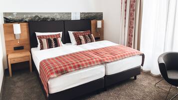 A double bed with a red plaid bedspread, two nightstands with lamps, a black chair, and a headboard with a mountain mural.