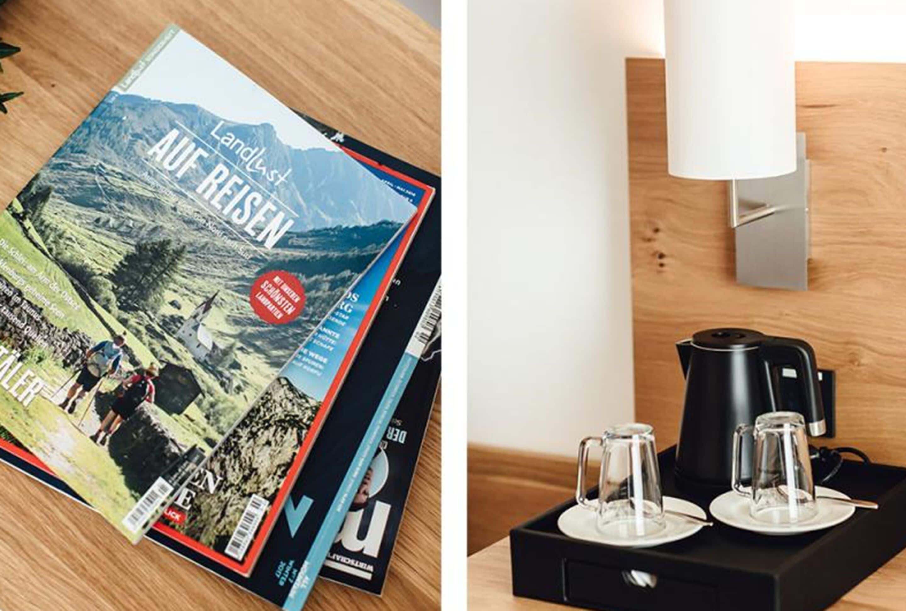 Una revista titulada "Landlust Auf Reisen" sobre una superficie de madera, y una estación de café con hervidor y tazas sobre una bandeja negra.