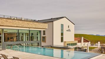 Un edificio moderno con piscina, asientos exteriores y vistas al campo.