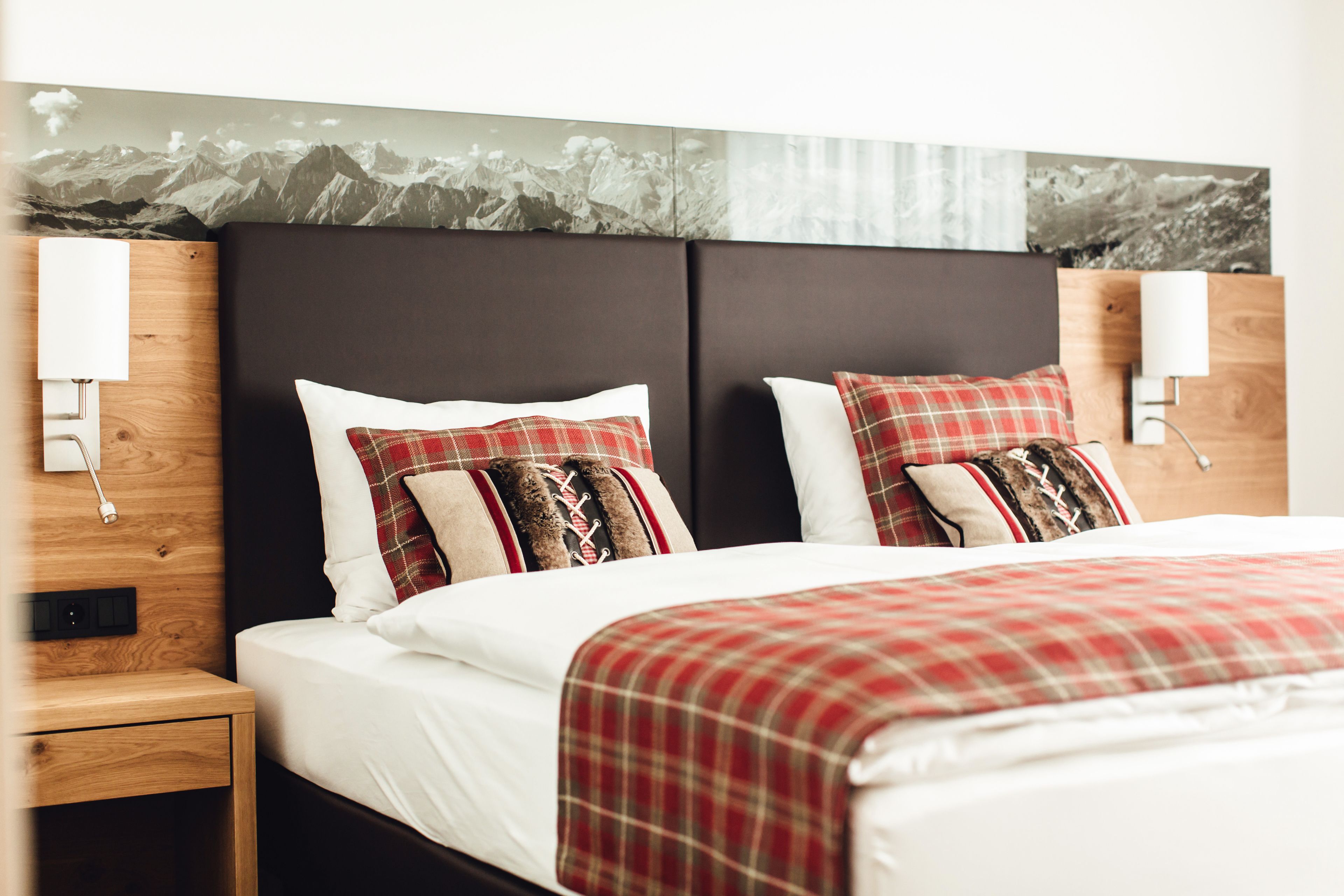 Habitación de hotel con una cama grande, dos mesitas de noche y un cabecero con vistas a la montaña.