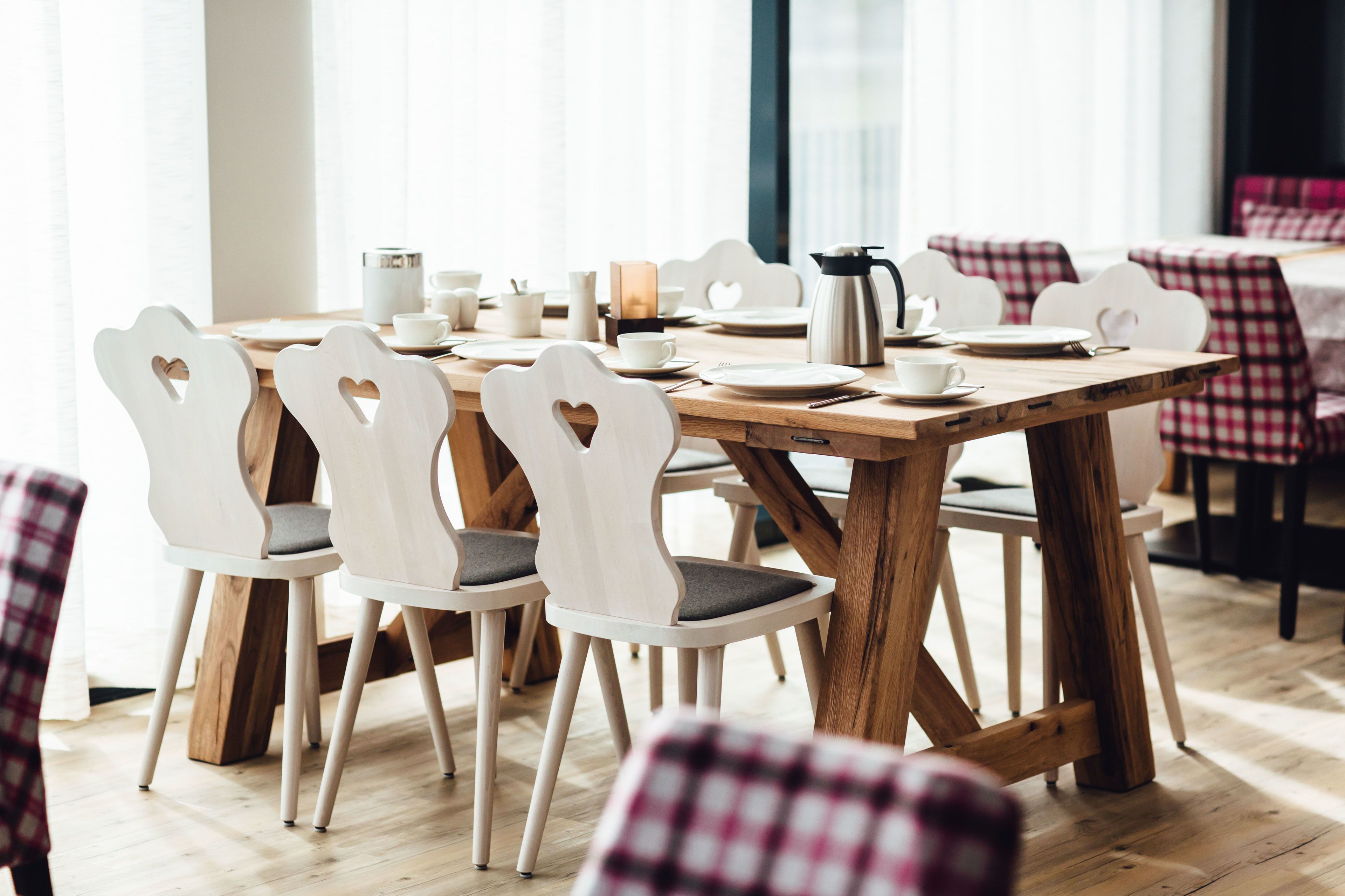 Un comedor con una mesa de madera, sillas blancas con forma de corazón y manteles a cuadros.