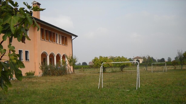 A building with a peach-colored facade, arched windows, and a small garden area. - Agriturismo Campi di Grano (Roncade)