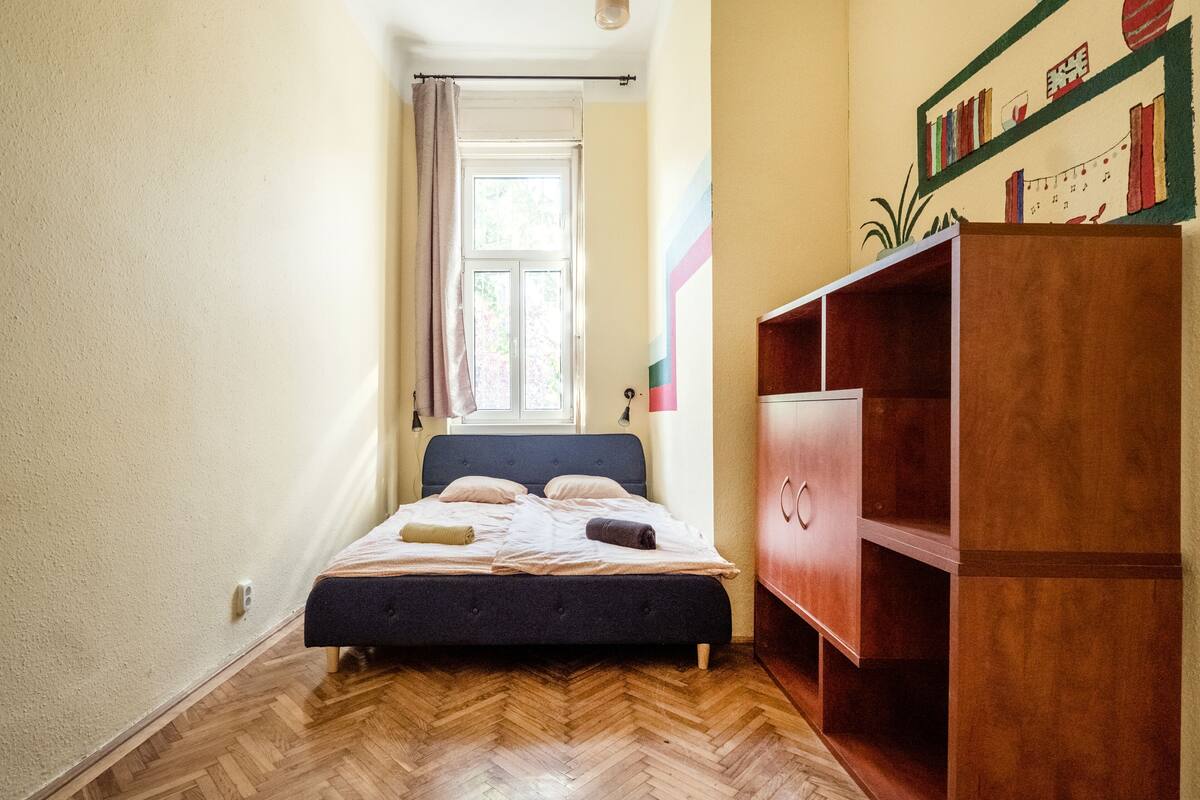 A bedroom with a bed, wooden floor, a window, and a wardrobe.