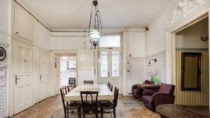 Een ruime eethoek met een lange houten tafel en stoelen, een hanglamp en uitzicht op de keuken door een geopende deur.