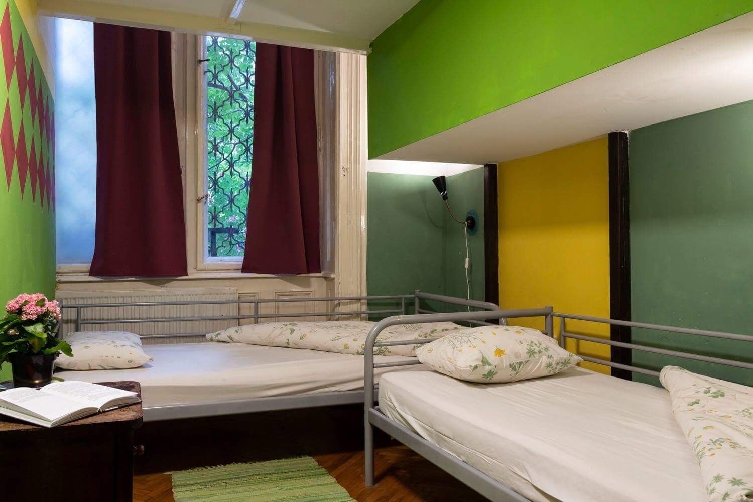 Habitación individual con ventana, radiador y mesita de noche con un libro.