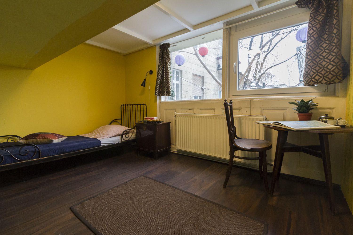A small, compact room with a single bed, a chair, a table, and a radiator.
