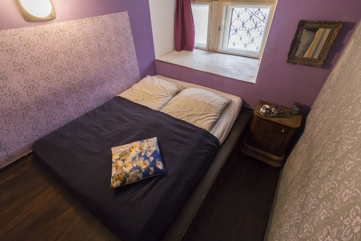 A bedroom with a bed, a nightstand, a window with a view, and a wall with a floral pattern.
