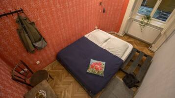 Un dormitorio pequeño con cama, una silla, una mesita con tazas y una ventana con vistas.
