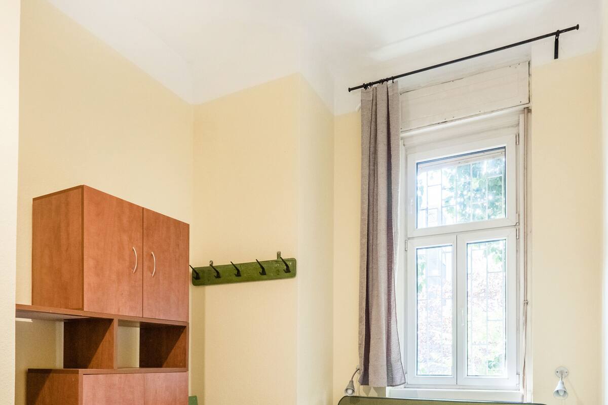 A bedroom with a green bed, wooden wardrobe, and a window with curtains.