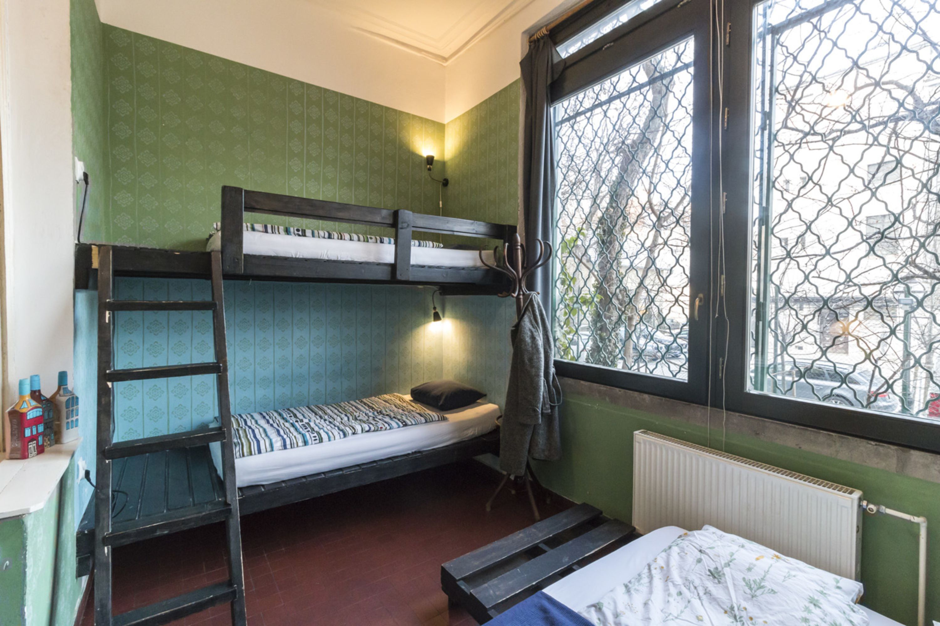 A bunk bed room with a ladder, a window with a metal screen, and a radiator.