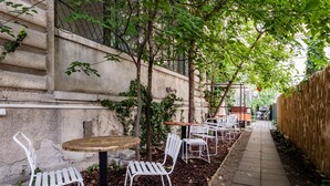 Een terras met tafels en stoelen, omgeven door bomen en een stenen muur.