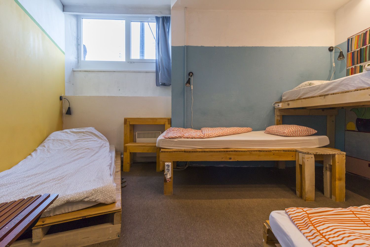 Quarto em dormitório com beliches, uma pequena cadeira de madeira, uma janela com cortina e um radiador.