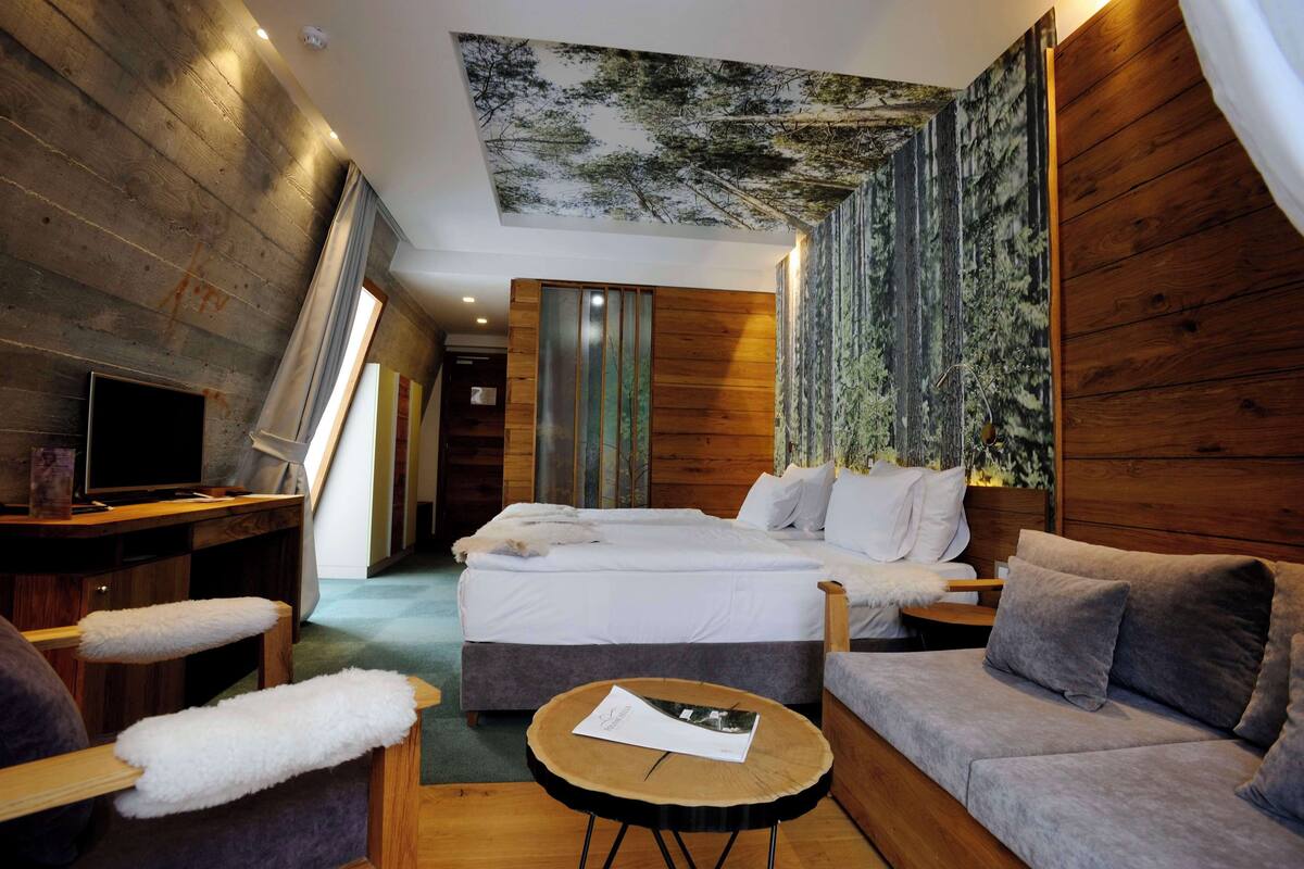 A modern hotel room with a large bed, a sofa, a small table, and a TV.