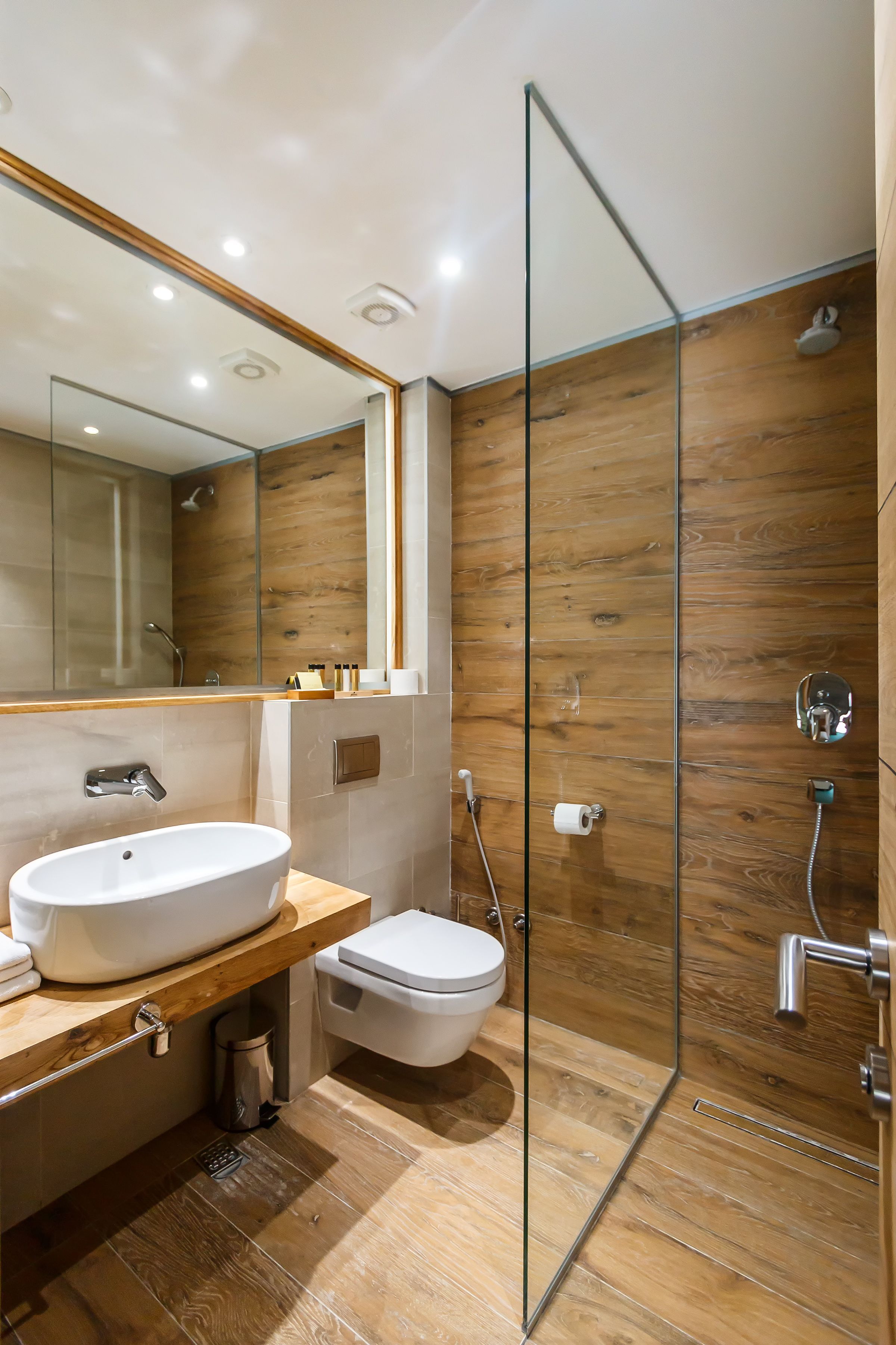 Een moderne badkamer met houten vloer, een glazen douchecabine, een witte wastafel en een toilet.