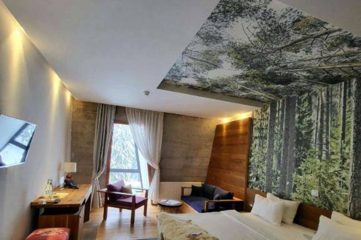 A modern hotel room with a large bed, a desk, a chair, and a view of trees through the window.