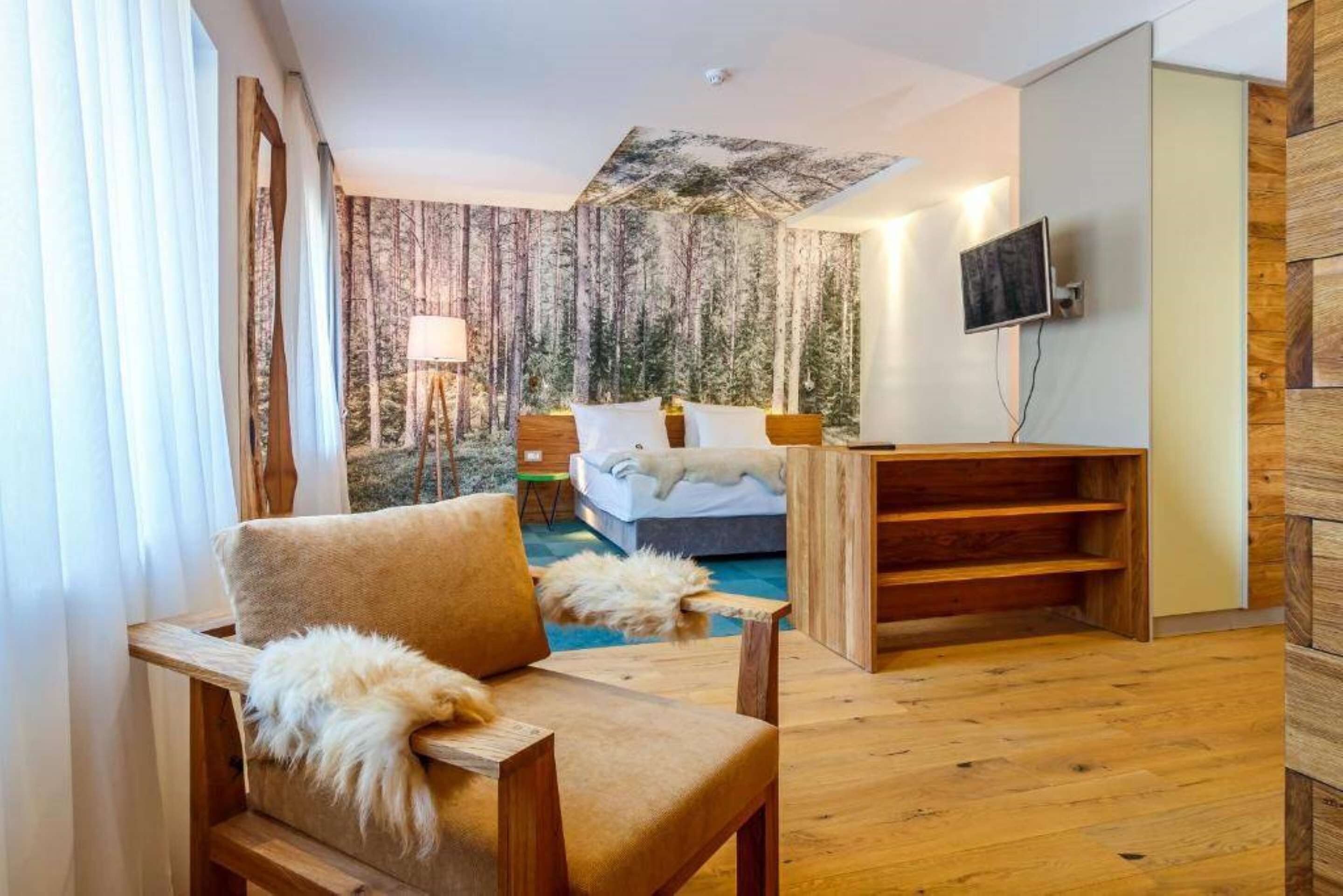 Una habitación moderna con cama, una silla de madera, un televisor y un ventanal con cortinas.