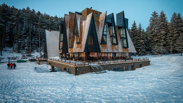 A modern building with a unique architectural design, featuring multiple levels and large windows, surrounded by a snowy landscape and dense forest. - Pino Nature Hotel, BW Premier Collection (Sarajevo)