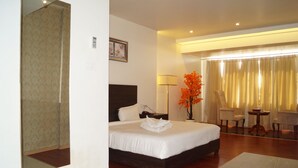 A hotel room with a large bed, a bedside table, a chair, a table with a vase of flowers, and a mirror. - Shiva Inn (Bilha)