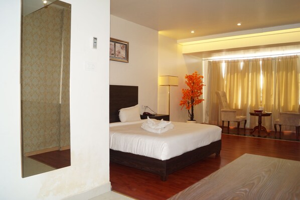 A hotel room with a large bed, a bedside table, a chair, a table with a vase of flowers, and a mirror.