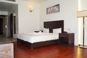 A hotel room with a wooden bed, bedside table, lamp, and a framed picture on the wall.