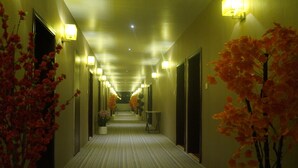 A hotel hallway with a striped carpet, wall-mounted lights, and potted plants. - Shiva Inn (Bilha)