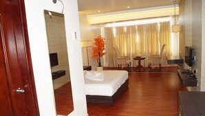 A hotel room with a bed, a desk, a chair, a TV, and a large window with curtains. - Shiva Inn (Bilha)