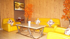A room with yellow sofas, a wooden table, and a vase with orange flowers. - Shiva Inn (Bilha)
