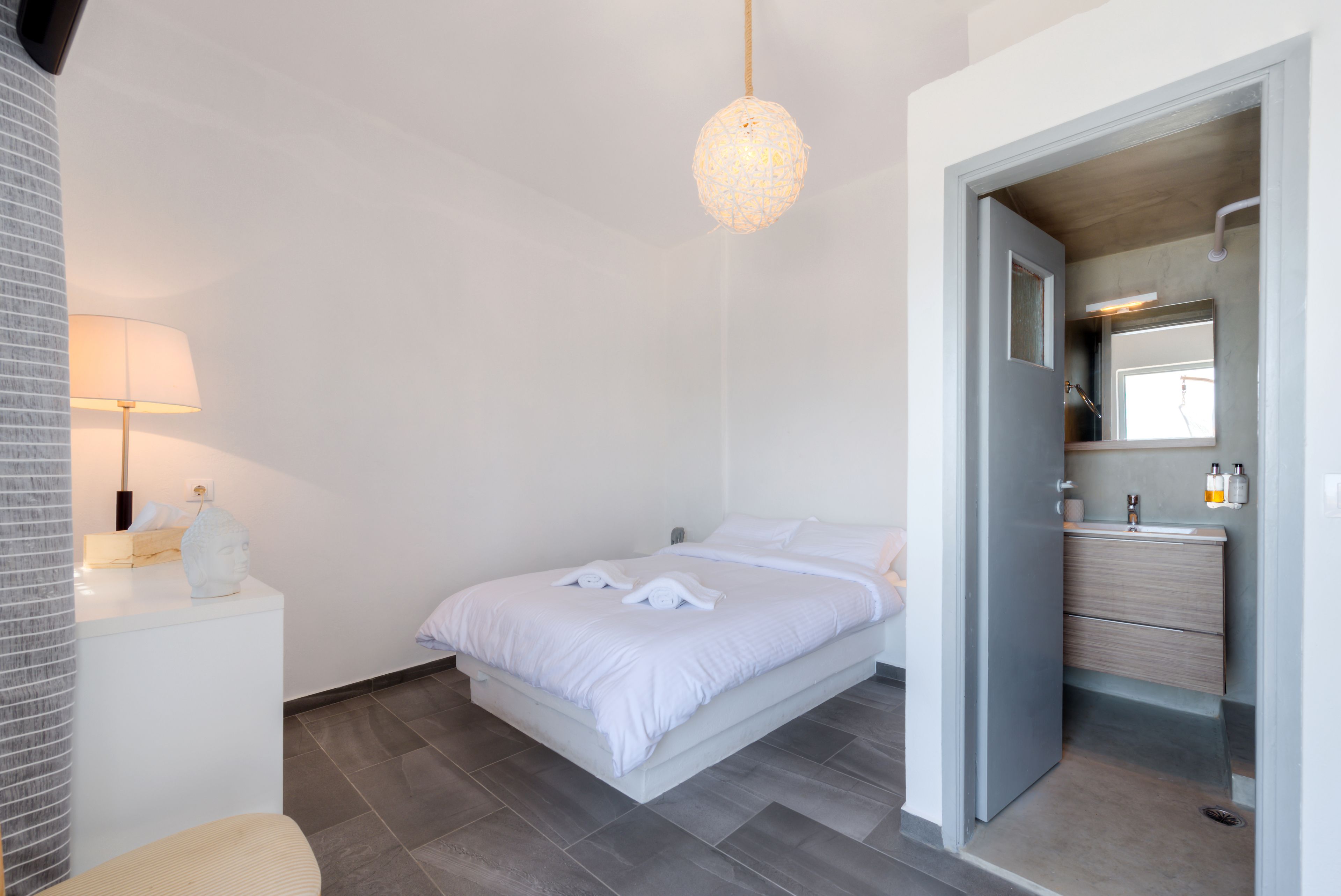 Una camera da letto moderna con un letto, comodino, lampada e bagno con specchio e lavandino.