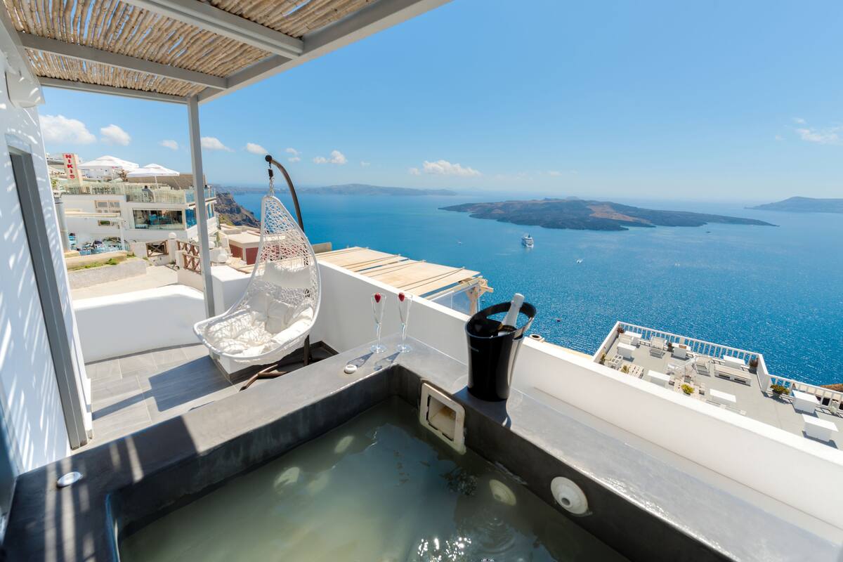 A rooftop terrace with a hot tub, a bottle of champagne, and a view of the sea.