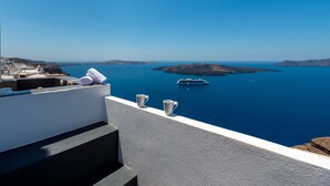 A terrace with a view of the sea, a boat, and a distant island. - Katris Apartments (Santorini)