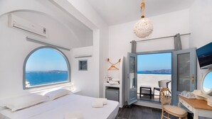 A modern hotel room with a large bed, a desk, a chair, and a view of the sea. - Katris Apartments (Santorini)