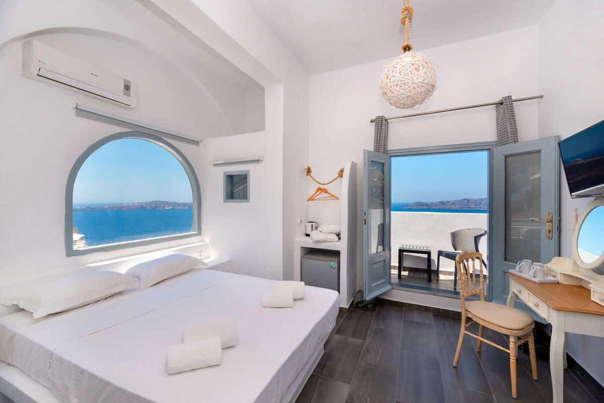 A modern hotel room with a large bed, a desk, a chair, and a view of the sea.