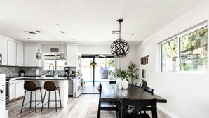 Eine moderne Küche mit weißen Schränken, einer Holzeile mit Barhocker und einem Essbereich mit einem dunklen Holztisch und Stühlen.